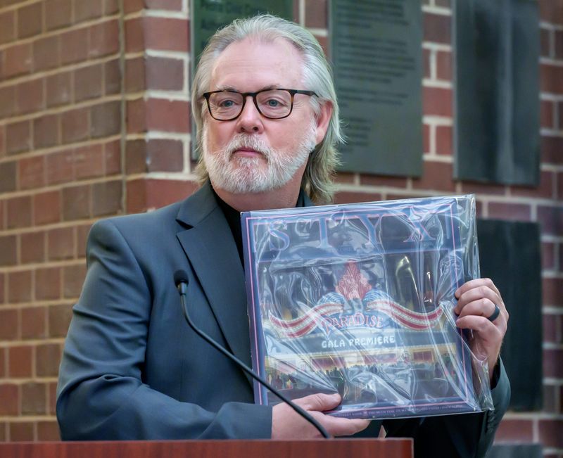 Peoria Civic Center general manager Rik Edgar shows off the inspiration for the design of the new Prairie Home Alliance Theater marquee, the cover of his cherished copy of Styx's 1981 album Paradise Theatre, during a dedication ceremony Thursday, Aug. 21, 2025 at the theater entrance.