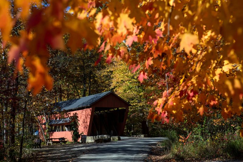 There orange glow from the fall foliage frames the covered bridge along the walking path at Alley Park on October 24, 2024, in Lancaster, Ohio.
