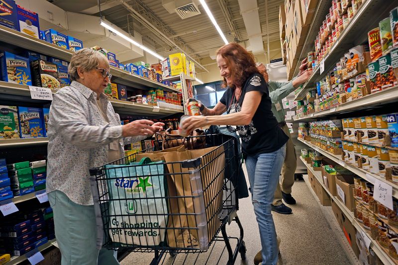 Pantry client Deb Flynn,center, 70 of Marshfield has relied on the pantry for 13 years. Volunteers Maureen Carey and Lew Verash of Marshfield helps her with her monthly supply.The Marshfield Food Pantry braces for more than the usual number of clients with the loss of SNAP benefits across the country during the government shut down on Tuesday November 4, 2025