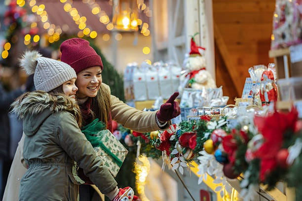 Mother and daughter browse a cheerful Christmas market, discovering gifts and decorations as twinkling lights and seasonal decor create a warm, joyful holiday atmosphere.