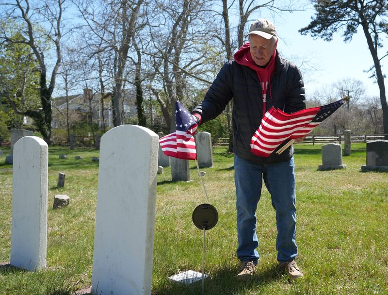 J. David Bowie, chair of the Dennis Cemetery Advisory Committee, places a flag at the headstone of an American Revolution soldier buried in the Dennis Village Cemetery. 
Betsy Ross flags have been placed on graves of the soldiers of the American Revolution at the Dennis Village Cemetery. The flags were placed on Tuesday ahead of the Hometown Heroes event on May 16. The Dennis Historical Commission is hosting the event that will include a special plaque dedication.
In honor of the 250th anniversary of American Independence, the town of Dennis will be dedicating the memorial plaque to the the soldiers of the 27 families who fought during the American Revolution.
The event will be held from 2:30 p.m. to 4 p.m. May 16, Armed Services Day. 
In all of the town's cemeteries there are 115 American Revolution soldiers, said Dennis Historical Commission chair Diane Rochelle, who was out helping with the flag placement. 
Photo taken May 5, 2026