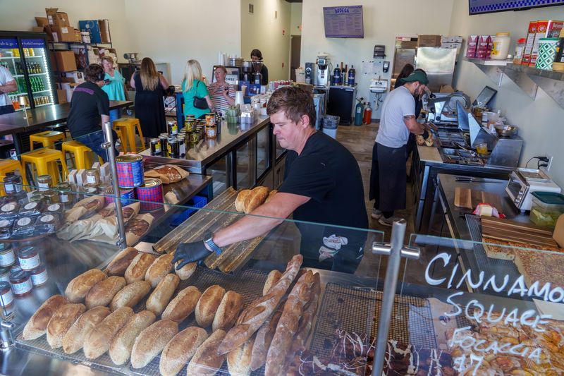 Ardor Hospitality owner Cody Scogin restocks the shelves with freshly-baked bread at his newest venture Bodega by Ardor, a small grocery store and gourmet deli at 4500 N. Prospect Road, Suite 102 in Peoria Heights..