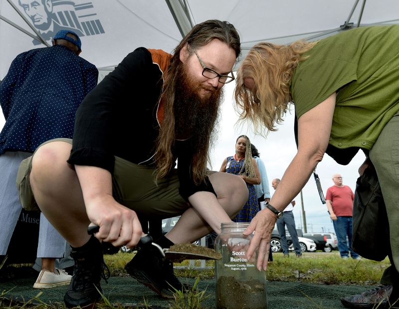 Andrew Schneider of Springfield, left, scoops soil into a jar marked for Scott Burton as part of a soil collection ceremony coordinated by the Abraham Lincoln Presidential Library and Museum Aug. 14, 2026. Burton was one of two black men lynched during the Springfield 1908 Race Riot. The jars will be on display at the ALPLM before going to the Equal Justice Initiative Legacy Museum in Montgomery, Alabama.