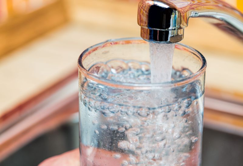 Water is pictured flowing into a glass from a kitchen faucet.
