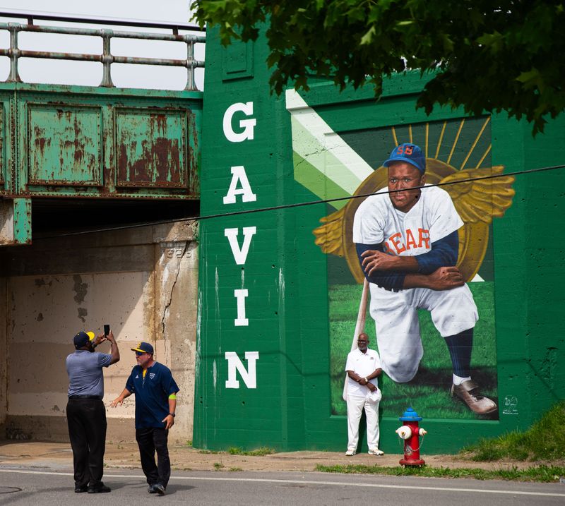 Riley High School athletic director, Seabe Gavin, Jr., gets his photo taken in front of a mural of his father, Seabe Gavin, Sr., during the unveiling of murals at a new public baseball field, Foundry Field, on Monday, May 20, 2024, in South Bend.