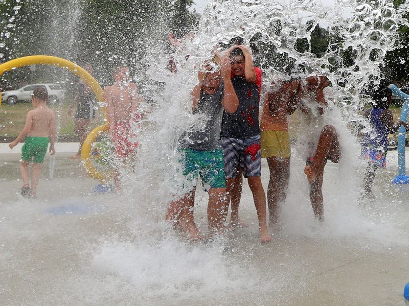 Children get wet underneath the water-filled bucket feature Tuesday, July 9, 2024, at Rose Park on Mishawaka’s West End. The city unveiled the first phase of the park’s three-phase restoration and transformation.