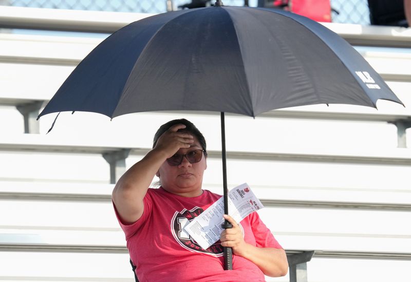 A New Palestine High School fan stays cool under an umbrella before a game against Decatur Central High School on Friday, Aug. 30, 2024, at New Palestine High School.