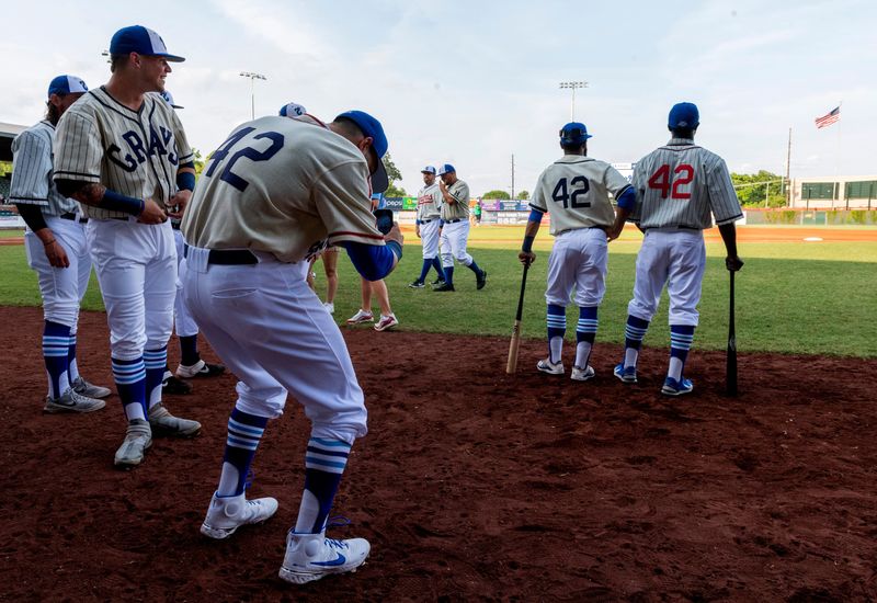 Tyler Spring, left, takes a photo of his teammates JR Davis, center, and Josh Henderson, right, pose as the Evansville Otters baseball team wear replica jerseys to pay tribute to the Negro Leagues on Juneteenth Saturday evening, June 19, 2021.