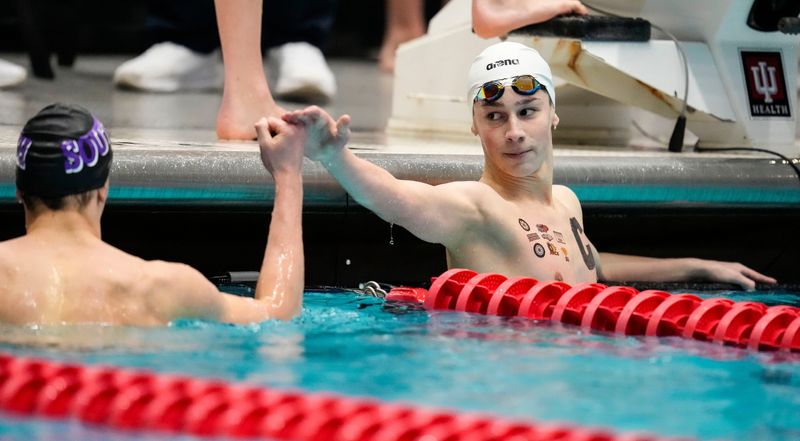 Carmel's Carter Hadley high fives Bloomington South's Peter Kovacs competes in the 100 yard freestyle Friday, Feb. 28, 2025, during the IHSAA boys state swimming preliminaries at the IU Natatorium at IU Indianapolis.