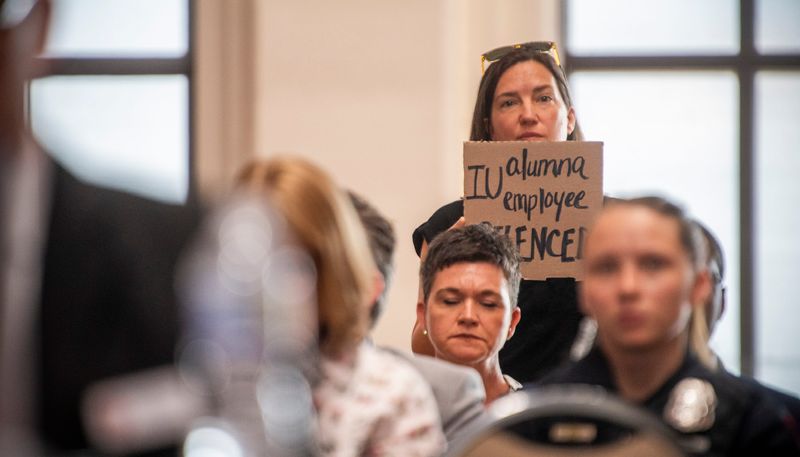 A protester holds a sign during the Indiana University Board of Trustees meeting in the Henke Hall of Champions at Memorial Stadium at Indiana University - Bloomington on Thursday, June 12, 2025.