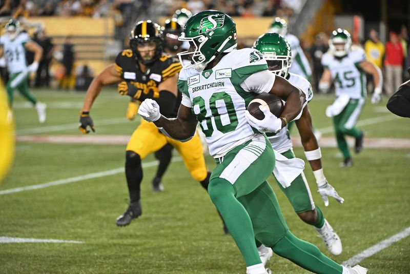 Jun 16, 2024; Hamilton, Ontario, CAN; Saskatchewan Rough Riders wide receiver Ajou Ajou (80) carries the ball in the fourth quarter against the Hamilton Tiger Cats at Tim Hortons Field. Mandatory Credit: Gerry Angus-USA TODAY Sports