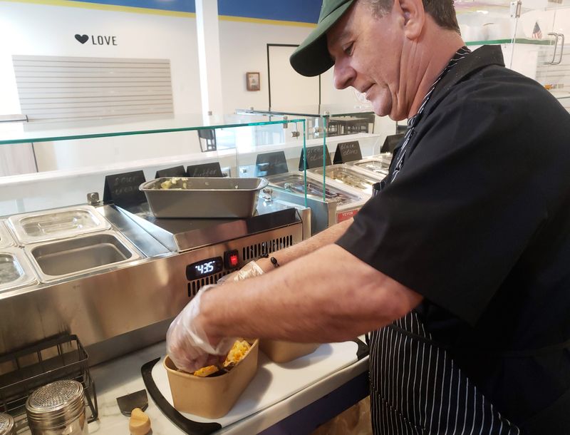Erol Sinan adds ingredients to a baked potato at Spudshacks, a new restaurant in downtown Bloomington, on Thursday, Aug. 7, 2025.