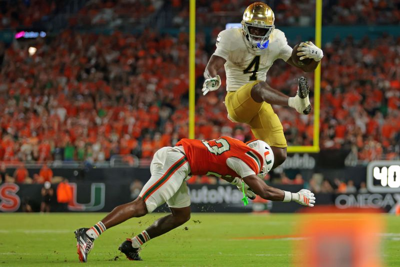 Aug 31, 2025; Miami Gardens, Florida, USA; Notre Dame Fighting Irish running back Jeremiyah Love (4) hurdles over Miami Hurricanes defensive back Dylan Day (23) during the third quarter at Hard Rock Stadium. Mandatory Credit: Sam Navarro-Imagn Images
