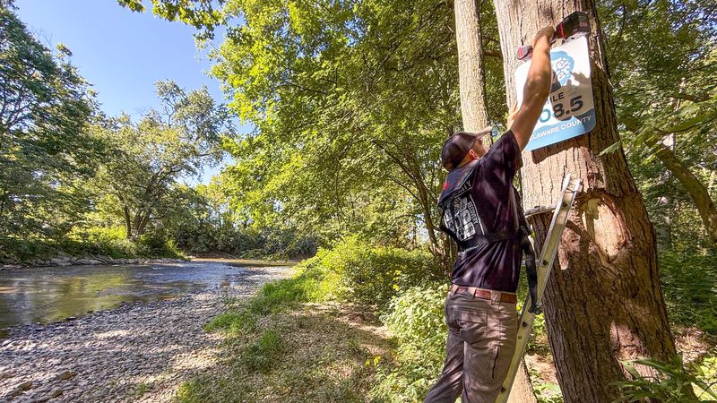 A volunteer installs one of 69 new White River mile marker signs — part of a Ball Brothers Foundation-funded safety project. The markers, integrated with Delaware County’s 911 system, will help emergency responders quickly locate and assist individuals along the river.