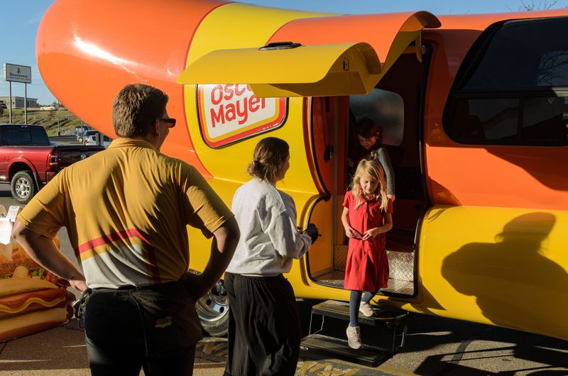 Oscar Mayer hotdogger Jack Cupit looks on as Audrianna Fuchs helps 6-year-old Mila Hertel and 4-year-old Isla Hertel tour the Wienermobile on Thurs., Nov. 13, 2025, outside a Schnucks grocery store on Evansville's West Side.