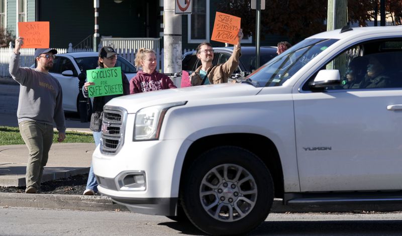 Participants hold out signs to passing cars during a protest calling for pedestrian and bicyclist safety Sunday, Nov. 23, 2025, on Massachusetts Avenue in Indianapolis.