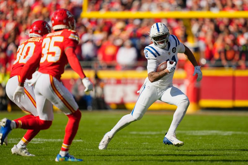 Nov 23, 2025; Kansas City, Missouri, USA; Indianapolis Colts wide receiver Michael Pittman Jr. (11) runs against Kansas City Chiefs cornerback Chris Roland-Wallace (30) and cornerback Jaylen Watson (35) in the first quarter at GEHA Field at Arrowhead Stadium. Mandatory Credit: Jay Biggerstaff-Imagn Images