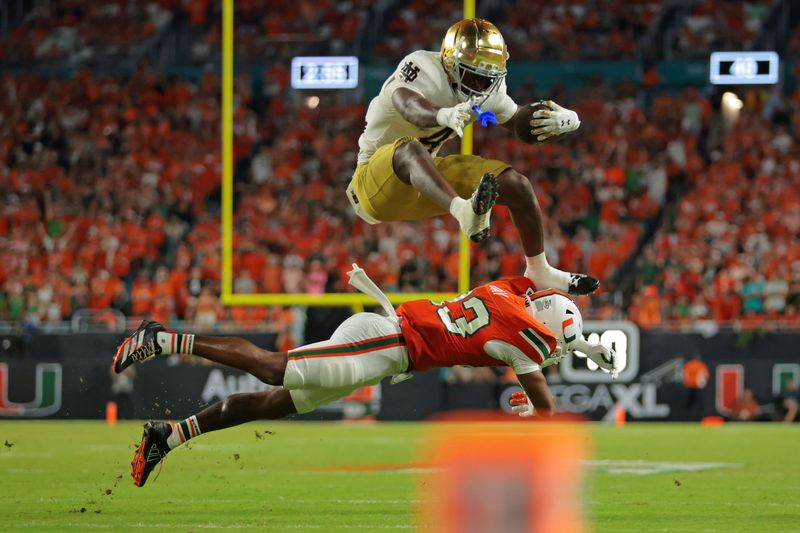 Aug 31, 2025; Miami Gardens, Florida, USA; Notre Dame Fighting Irish running back Jeremiyah Love (4) hurdles over Miami Hurricanes defensive back Dylan Day (23) during the third quarter at Hard Rock Stadium. Mandatory Credit: Sam Navarro-Imagn Images