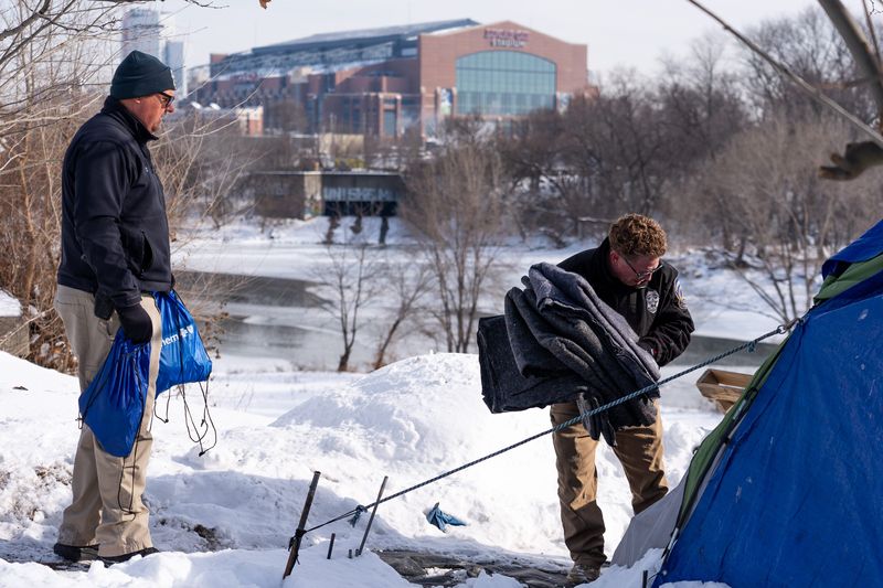 Indianapolis Metropolitan Police Department Patrolmen Phil Smiley (left) and Shawn Holmes, both with the homeless unit, carry blankets and food Thursday, Jan. 29, 2026, into a camp on the south side of the city.