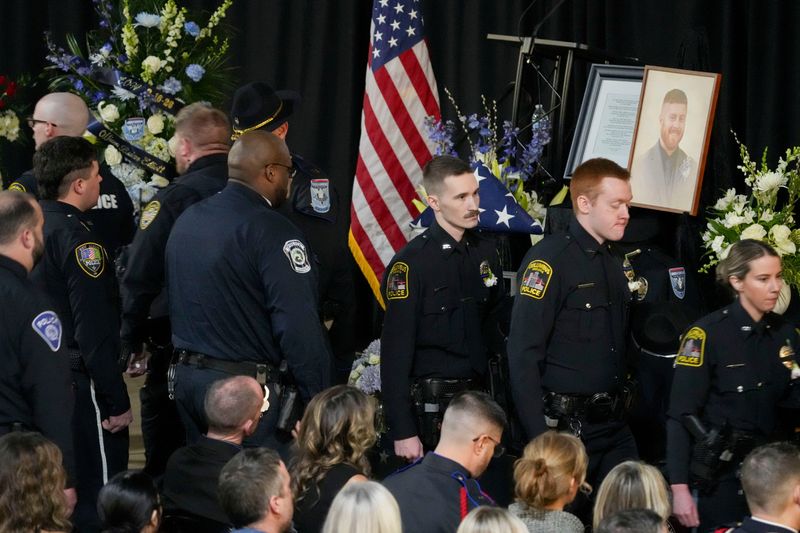 Officers stand by a memorial for fallen Beech Grove Police Officer Brian Elliott as people file in Monday, Feb. 23, 2026, ahead of his memorial service in the gymnasium at Beech Grove High School. Elliott was killed in the line of duty Feb. 16, while responding to a disturbance call.