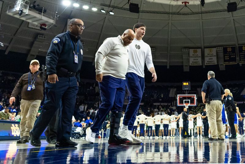 Feb 24, 2026; South Bend, Indiana, USA; Notre Dame Fighting Irish head coach Micah Shrewsberry is helped off the court while wearing a boot against the Duke Blue Devils after the game at Purcell Pavilion at the Joyce Center. Mandatory Credit: Michael Caterina-Imagn Images