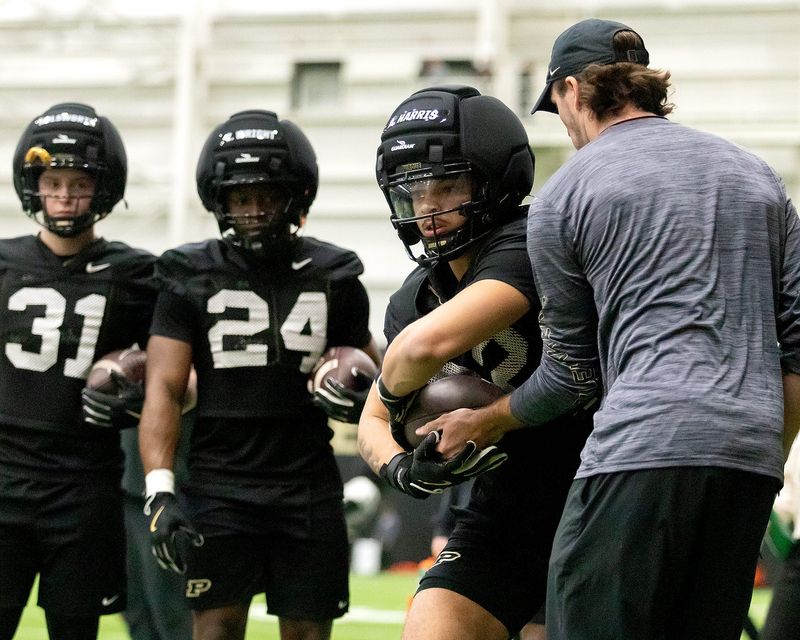 Junior running back Antonio Harris, right, grabs the ball from a coach while freshman running back Izaiah Wright, center, and sophomore running back Carter Holsworth watch the drill on Tuesday, March 3, 2026, at The Mollenkopf Athletic Center in West Lafayette, Ind. In the 2025 season Harris appeared in all 12 games with two starts and recorded 69 rushes for 305 yards and two touchdowns.