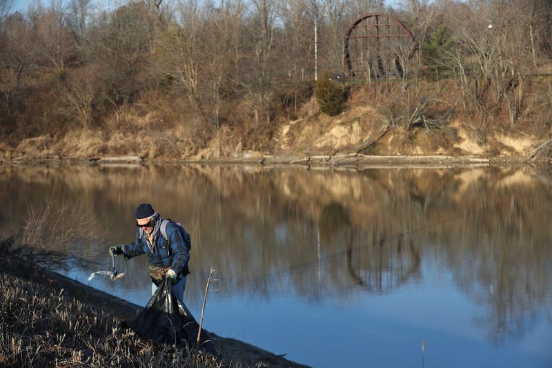Mike Brunette picks up trash at Eagle Creek Park Reservoir, Tuesday, Dec. 14, 2021 along 56th Street in Indianapolis. He volunteers his time cleaning in several of the city's parks. The Galyan's Bear statue can be seen in the distance.