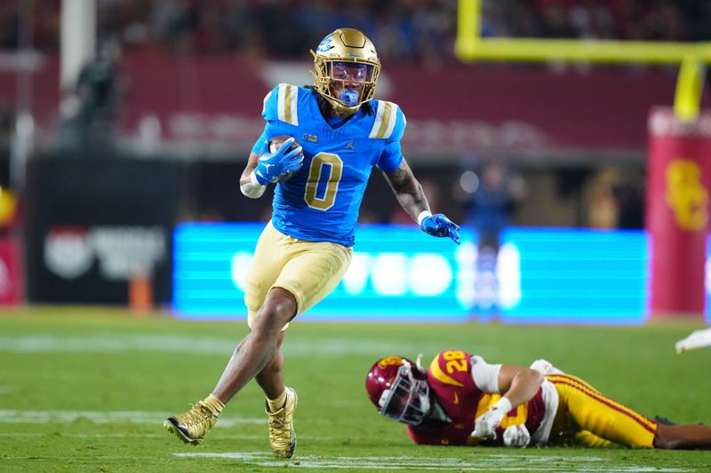 Nov 29, 2025; Los Angeles, California, USA; UCLA Bruins running back Jalen Berger (0) carries the ball against Southern California Trojans safety Kennedy Urlacher (28) in the first half at United Airlines Field at Los Angeles Memorial Coliseum. Mandatory Credit: Kirby Lee-Imagn Images