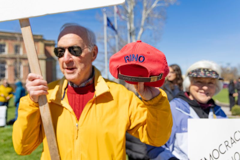Cliff Yehle of Union, Michigan, who considers himself a life-long Republican and can remember voting for Eisenhower, holds up a RINO (Republican in Name Only) hat to describe himself now during his first No Kings march Saturday, March 28, 2026, in Goshen. He also had a sign that said, "Wake Up America!"