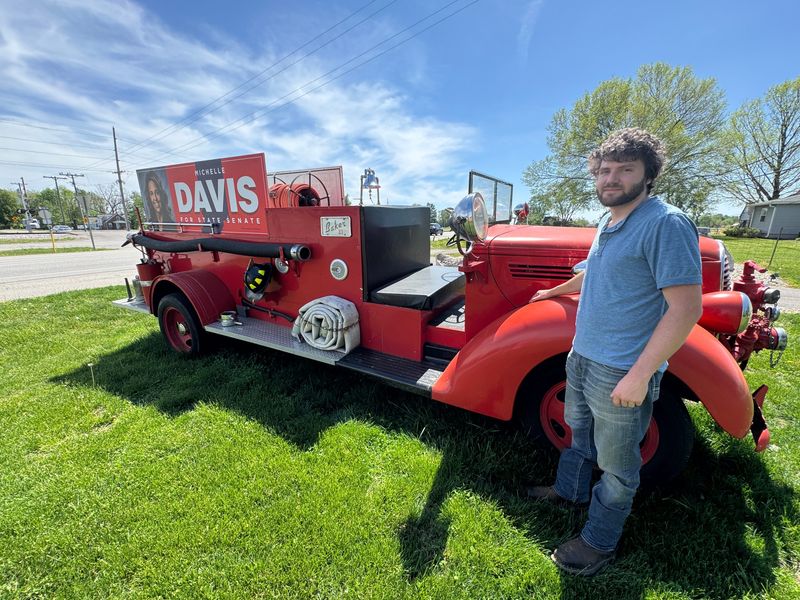 24-year-old Alex Kizer stands in front of a vintage fire truck with a campaign sign for State Rep. Michelle Davis, R-Whiteland, who's running for state senate in 2026, outside his Columbus home.