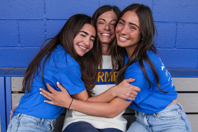 Eighth grade Carmel student Alex Kleiner and sister and senior Jayden Kleiner hug their mother and head softball coach Stephanie Kleiner on Thursday, May 7, 2026, at Cherry Tree Softball Complex in Carmel.