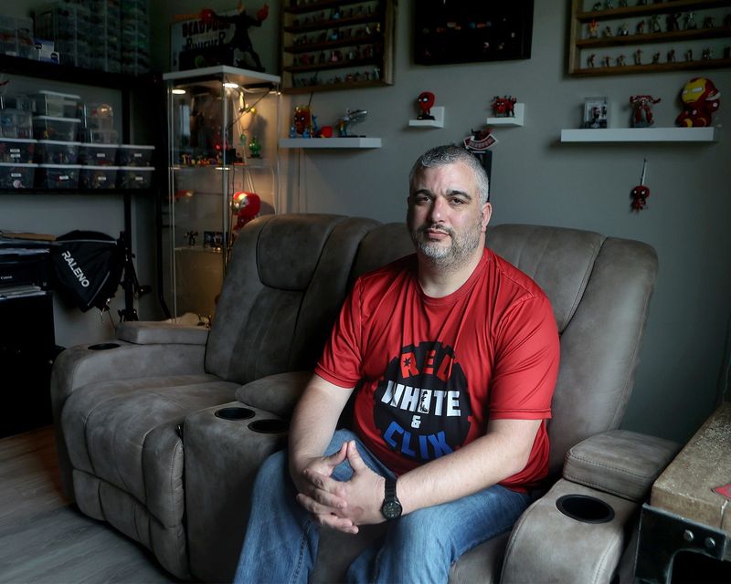 Wes Robertson sits in his home office before his superhero figurines.