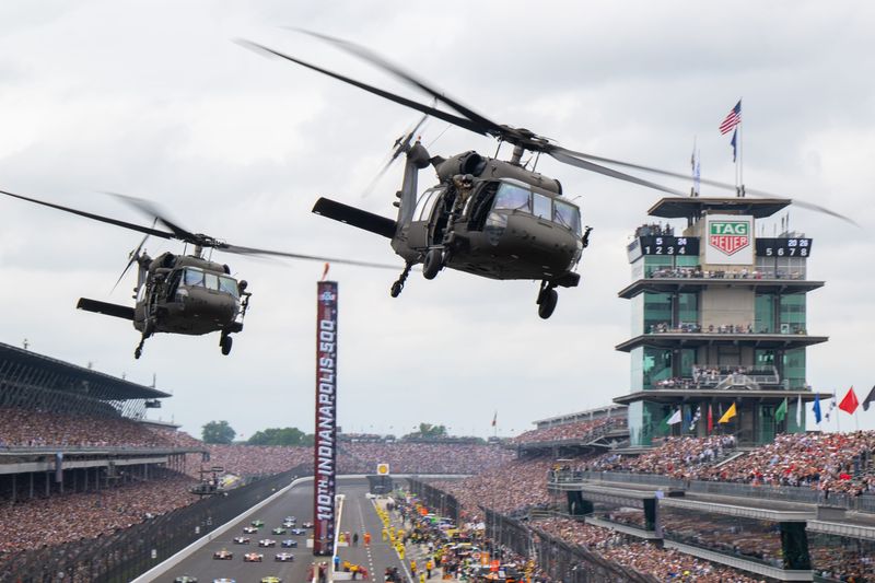 Military helicopters escort the field of competitors on a pace lap Sunday, May 24, 2026, during the 110th running of the Indianapolis 500 at Indianapolis Motor Speedway.