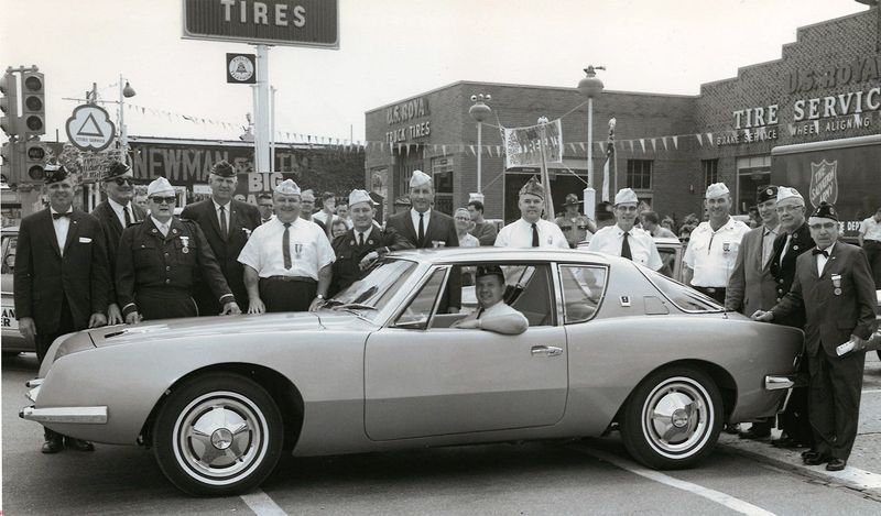 American Legion officials pose with an early Studebaker Avanti at start of parade during Indiana state American Legion convention in South Bend on July 14, 1962. Sign on Newman & Altman Packard showroom can be seen in background.