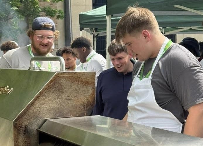 Notre Dame freshman offensive lineman Sullivan Garvin (r) shows off his culinary skills in the 2025 "Grill and Chill" competition for football recruiting director Carter Auman (center) and fellow Irish lineman Ben Nichols (left).