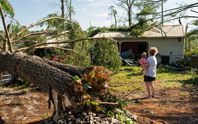 Holding her grandchild, Jacque Huffman walks out from her Buskirk home and garage on Thursday, June 18, 2026. The home was damaged by a tornado on June 17.