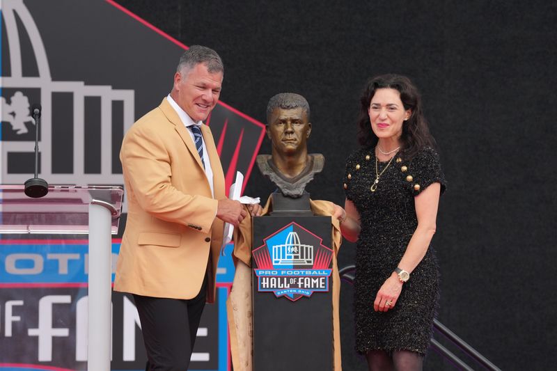Aug 8, 2026; Canton, OH, USA; Pro Football Hall of Fame enshrinee Adam Vinatieri presented by Indianapolis Colts co-owner Carlie Irsay-Gordon during the Class of 2026 enshrinement ceremony at Tom Benson Hall of Fame Stadium. Mandatory Credit: Kirby Lee-Imagn Images