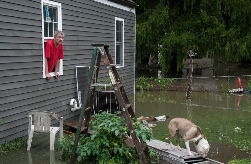 Norman Keller peeks out from the window of his house as it sits surrounded by floodwater Friday, Aug. 14, 2026, on West 6th Street in Anderson, Ind. Keller said he would stay as long as he could.