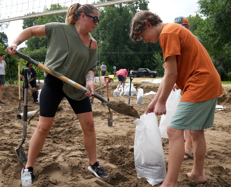 Abigail Erikson (left) and her son Ethan Erikson, 13, shovel sand from a volleyball court in Hohlt Park to keep back floodwater Sunday, Aug. 16, 2026, in Rocky Ripple.