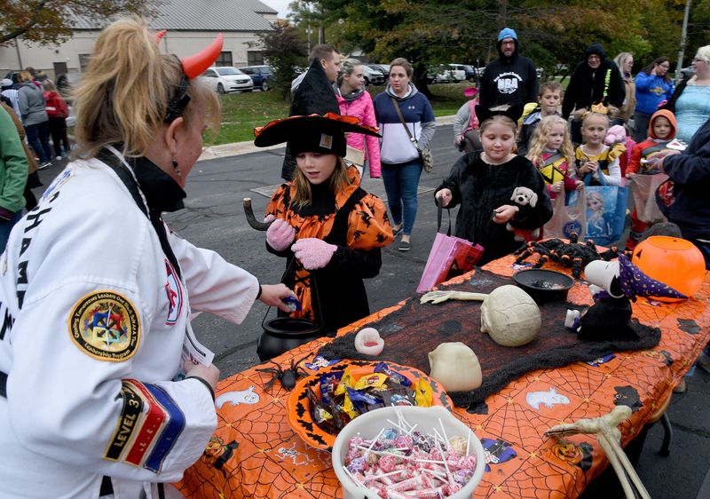 Mary Jo Feldkamp, head instructor for Temperance ATA Martial Arts, places candy into the bags of Autumn Walerius, then 7, and Kaleigh Mack, then 8, at a trunk-or-treat event at the Bedford Branch Library. Many trunk-or-treats and other fall activities are planned in Monroe County this October.