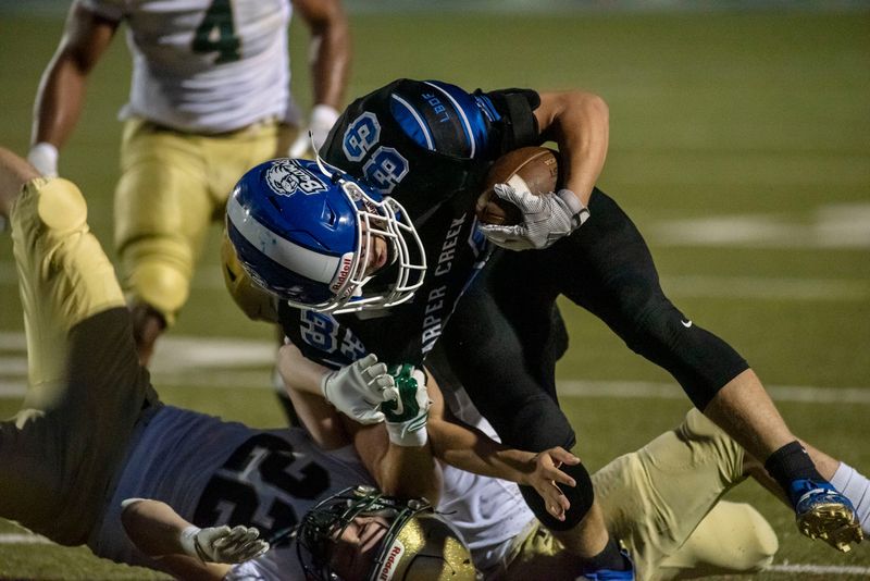 Lumen Christi senior Nicholas Wilson (22) and junior Joseph Lathers (12) tackle Harper Creek senior Julion McCray (33) on Friday, Oct. 1, 2021 at Harper Creek High School in Battle Creek, Michigan.