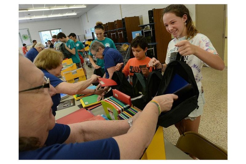 In a previous year, volunteer Seseana Franzen of DTE receives crayons from the youngest volunteer, Lily Johnson, then 8, a third-grader at Douglas Road Elementary with her grandmother, Kathleen Torony (center), and Pat LaBeau RSVP volunteers at Bedford Junior High School Thursday. This was for the Supplying Our Future Back Pack Coalition, a project led by the Salvation Army of Monroe County.