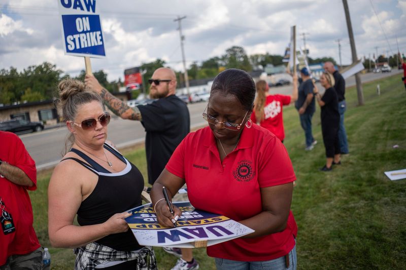 UAW Secretary-Treasurer Margaret Mock signs a strike sign for General Motors Corporation CCA Parts Division employee Amy Ross of Flint as workers stand on strike outside of General Motors Corporation Davison Road Processing Center in Burton on Friday, September 22, 2023.