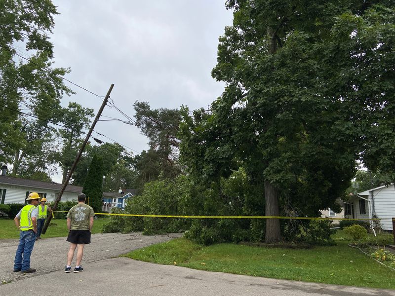 Patrick Morris, right, talks with Consumers Energy workers who are fixing power outages on Cypress Street in Haslett on Wednesday, Aug. 28, 2024. A large branch from Morris' 75-foot walnut tree fell during Tuesday's storm, blocking his street.