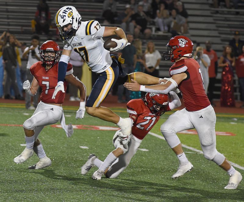 Lincoln Keyes of Saline is upended after a catch by Tanner Collett and Jax Jones (7) on Friday, Sept. 20, 2024.