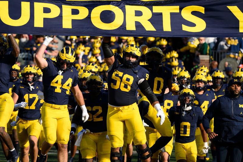 Michigan players leap to touch the banner as they run out of the tunnel for the start of a game against Oregon, at Michigan Stadium in Ann Arbor, Nov. 2, 2024.