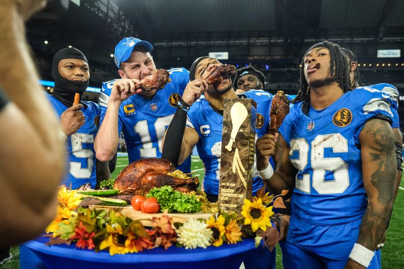 Detroit Lions quarterback Jared Goff (16), defensive tackle DJ Reader (98), wide receiver Amon-Ra St. Brown (14), running back Jahmyr Gibbs (26), linebacker Al-Quadin Muhammad (69) celebrate their win against the Chicago Bears with a turkey drumstick after winning 23-20 on Thanksgiving Day at Ford Field in Detroit on Thursday, Nov. 28, 2024.