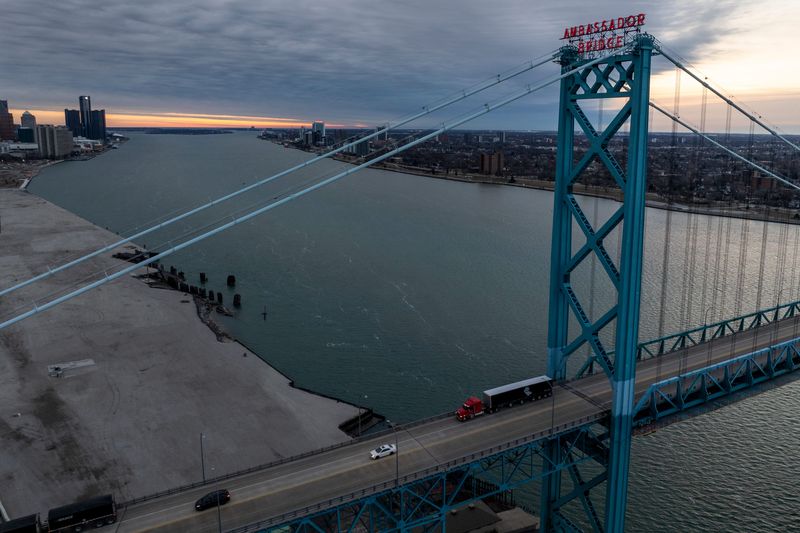 The sun rises over the Ambassador Bridge, illuminating the Detroit and Windsor skylines.