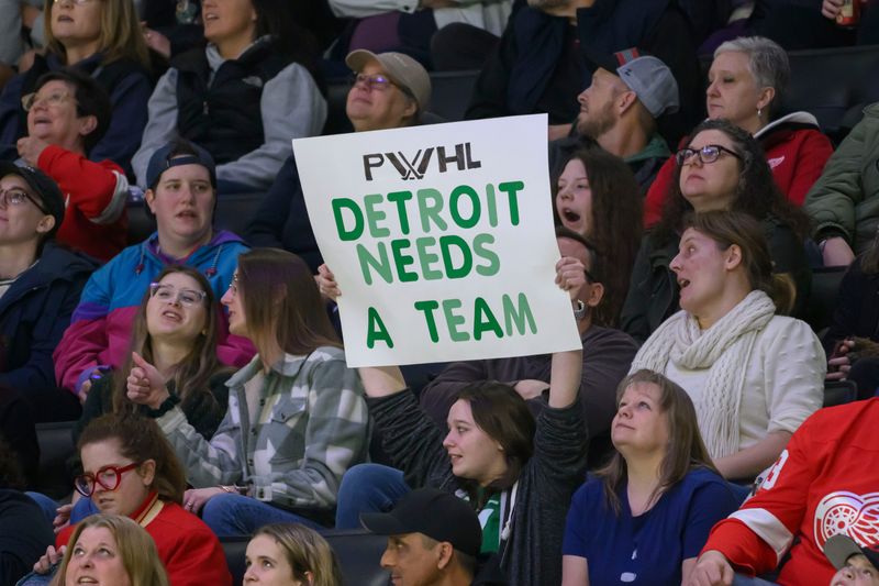 A fan holds a sign indicating a desire for an PWHL team to come to Detroit during the first period of a PWHL game between the New York Sirens and the Minnesota Frost, at Little Caesars Arena, in Detroit, March 16, 2025.