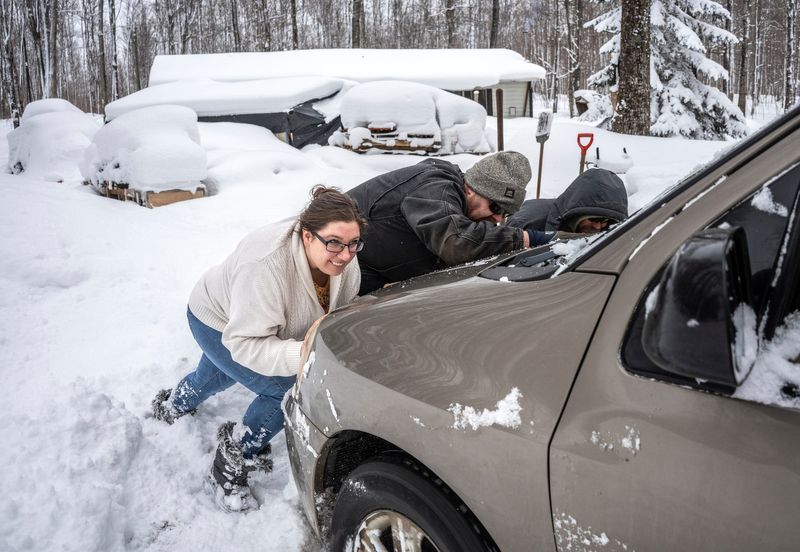 Registered nurse Monica Eriksen, left, helps try to push a van out of deep snow while making a visit to talk to Marie Woosck, 22, about her pregnancy while visiting her home in Munising on Friday, Feb. 7, 2025.